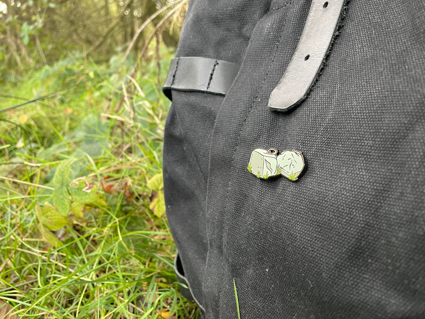 A closeup of a liftingstones.org Dinnie Stones enamel pin on a black backpack.